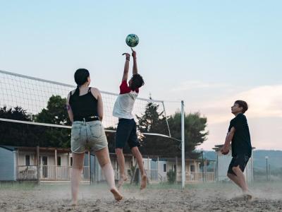Trois personnes jouent au volley-ball sur un terrain extérieur.