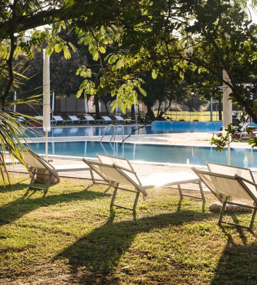 Piscina all'aperto circondata da lettini e alberi al tramonto.
