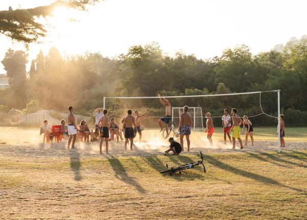 Junge Leute spielen Beachvolleyball bei Sonnenuntergang.