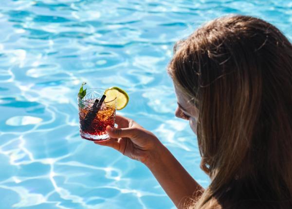 Frau mit Cocktail am Pool.