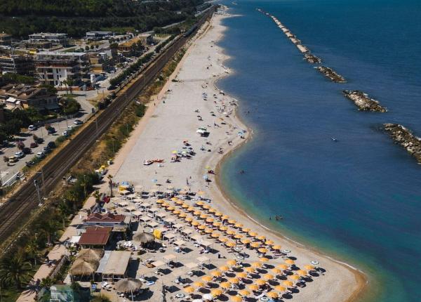 Beach with colorful umbrellas near railway and calm sea.
