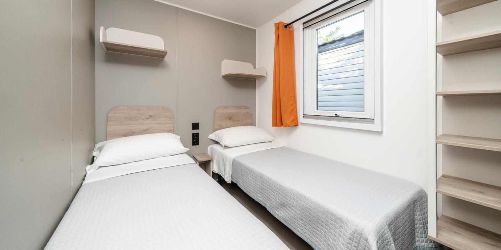 Einfaches Zimmer mit zwei Einzelbetten, Regalen und Fenster.