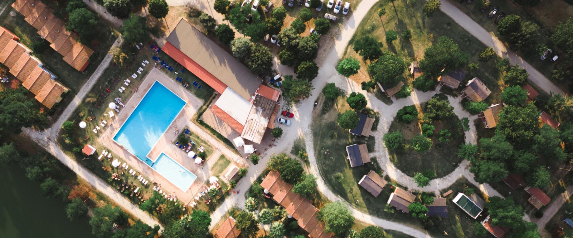 Vista aerea di un villaggio turistico con piscine e bungalow immersi nel verde.