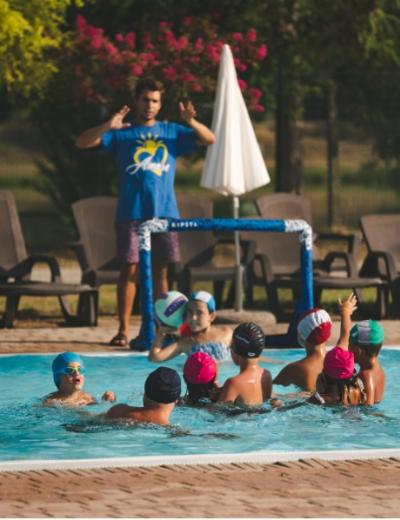 Bagnino in canotta rossa con la scritta 'SALVATAGGIO' di fronte a una piscina.