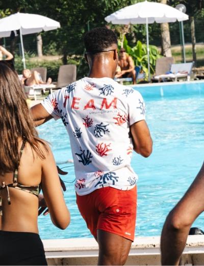 Persona con maglietta bianca e pantaloncini rossi vicino a una piscina.