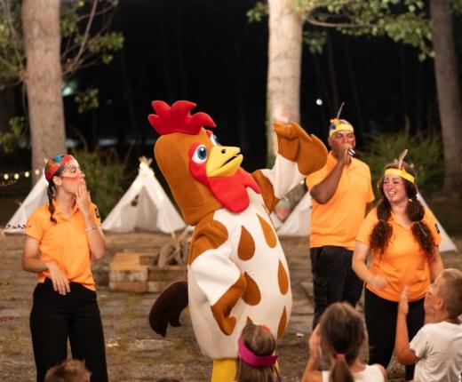 Festa serale all'aperto con una mascotte di gallo e animatori in costume.
