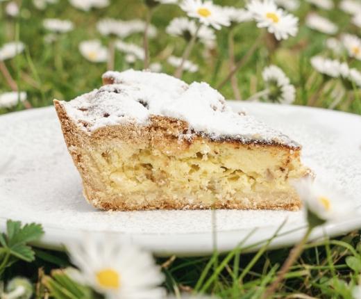 Fetta di torta ricotta e pere, spolverata di zucchero a velo, su prato fiorito.