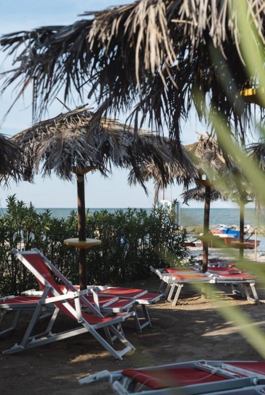 Spiaggia con lettini rossi e ombrelloni di paglia vicino al mare.