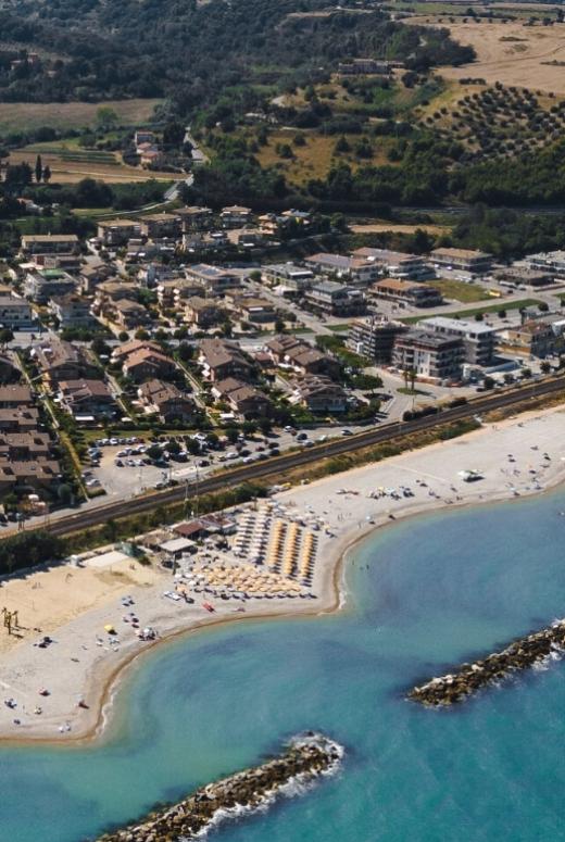 Vista aerea di una spiaggia con ombrelloni e un villaggio sullo sfondo.